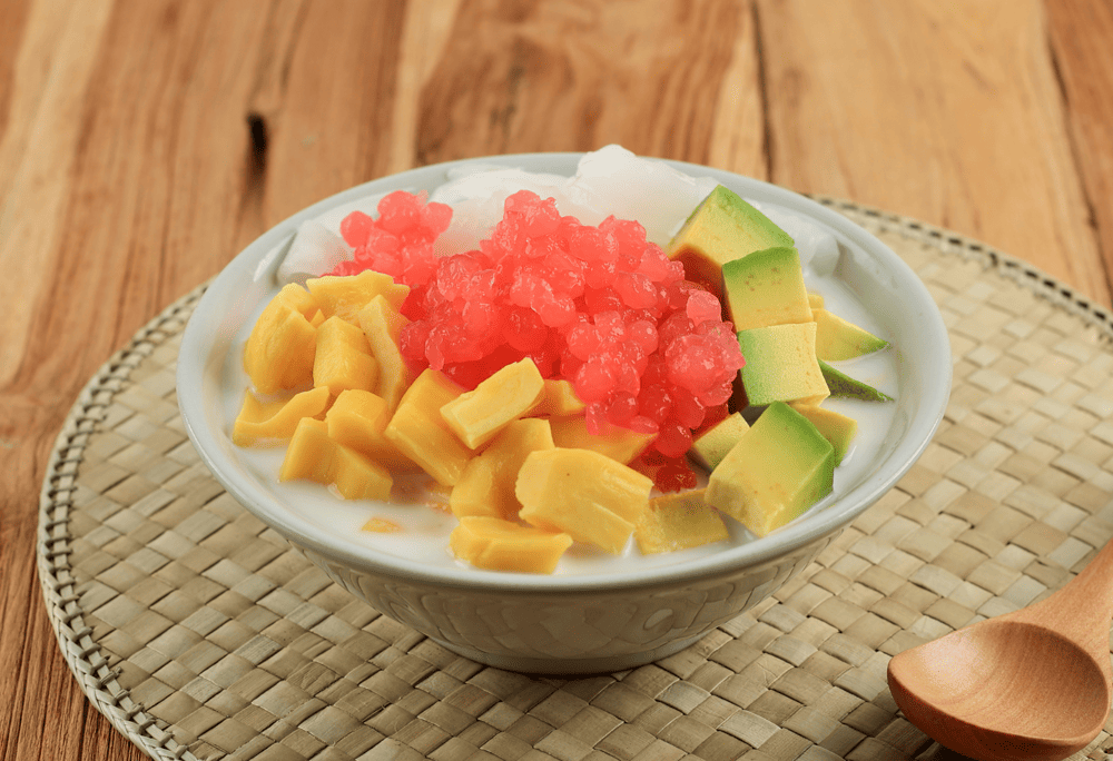 A rainbow bowl of hoa qua dam featuring colorful fruit pieces - pink dragon fruit, red watermelon, yellow mango, white longan, with crushed ice (Source: Canva)
